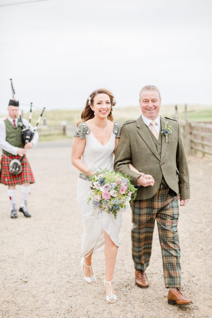 Bride and father of the bride walking bagpiper following