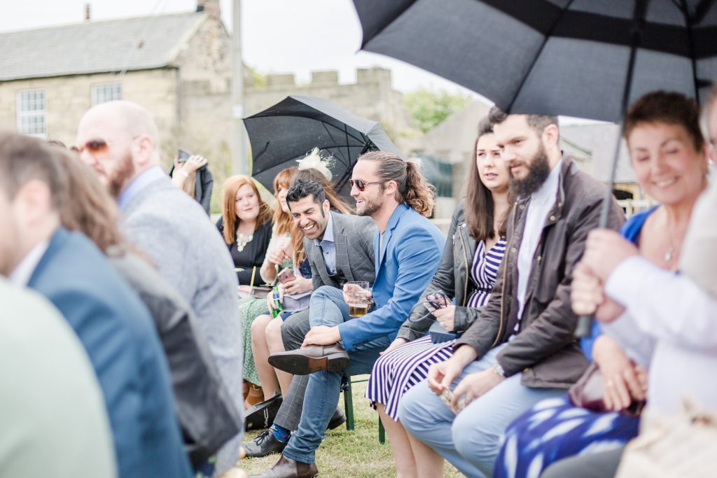 wedding guests sat on bench laughing under umbrella at festival wedding