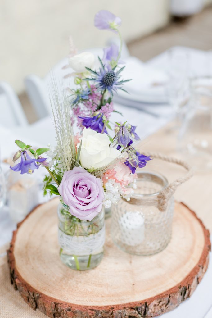 roses thistles and purple flowers in jam jars on wooden slices