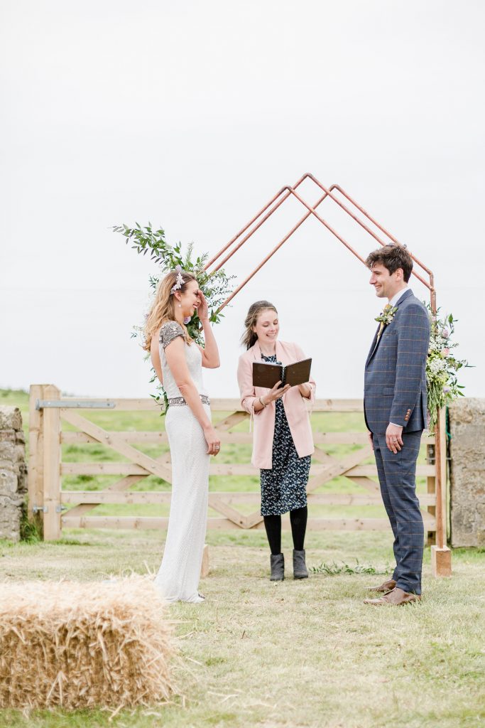 bride laughing with hand over face at alter with groom and celebrant copper arch