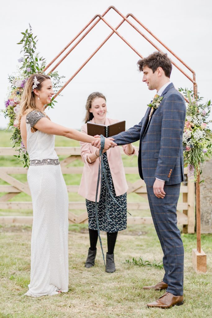 bride and groom holding hands for hand tying ceremony by celebrant