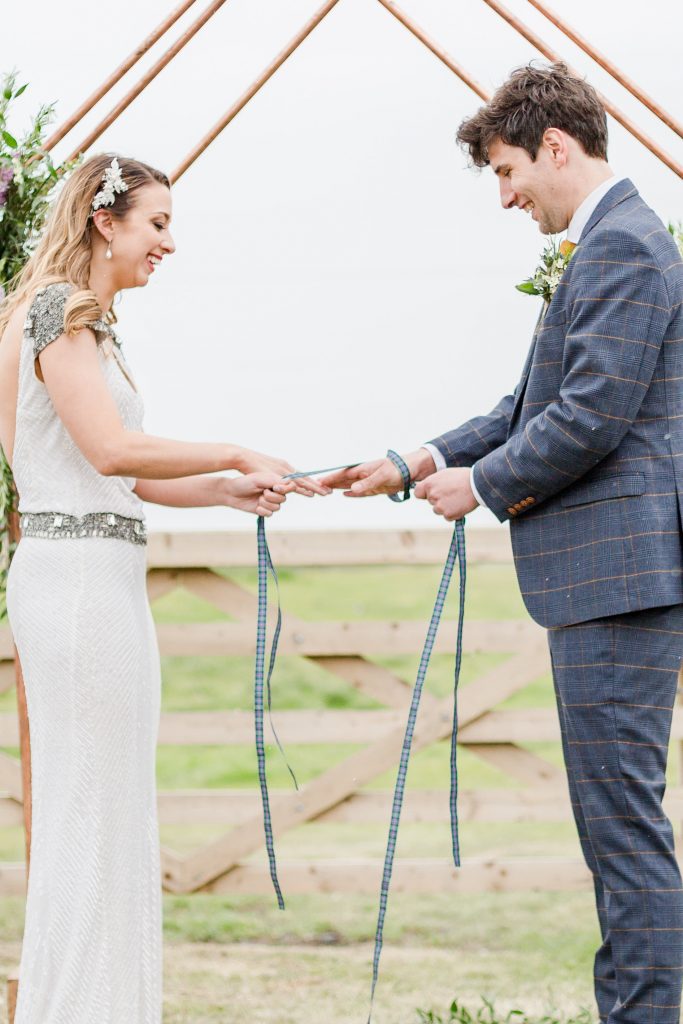 bride and groom pulling Scottish ribbon at hand tying ceremony laughing