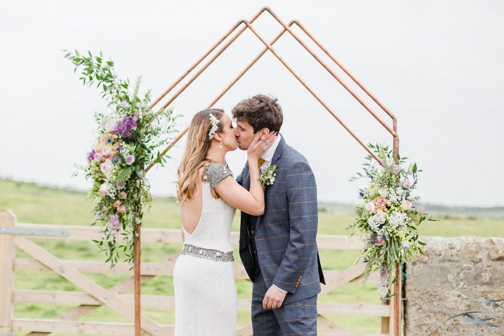 bride and groom kissing under copper arch at outside ceremony