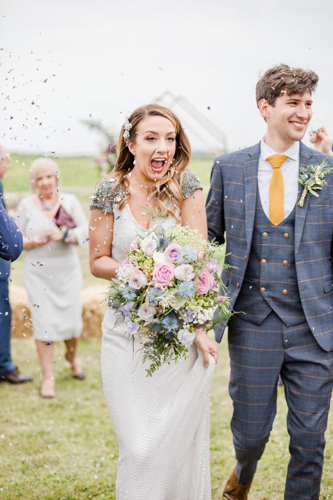 bride and groom walking under confetti in field