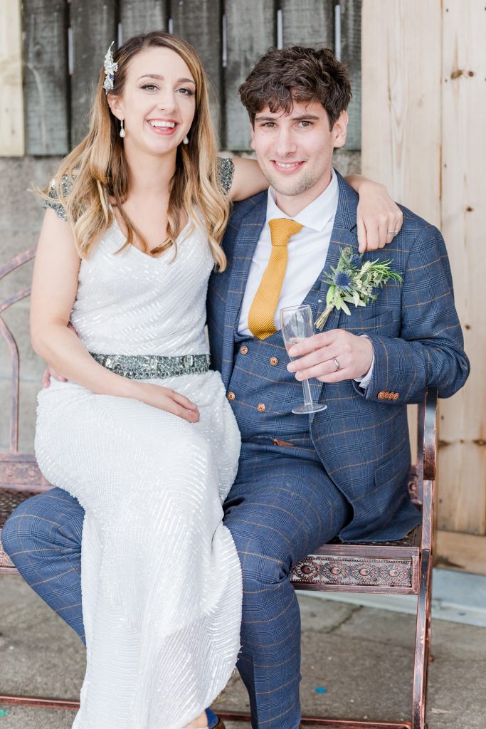 bride sat on grooms knee on bench infant of barn door