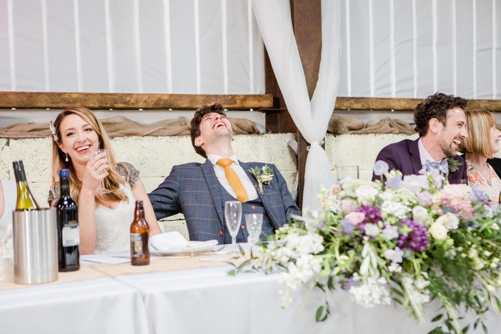 groom throwing head back in laughter at top table