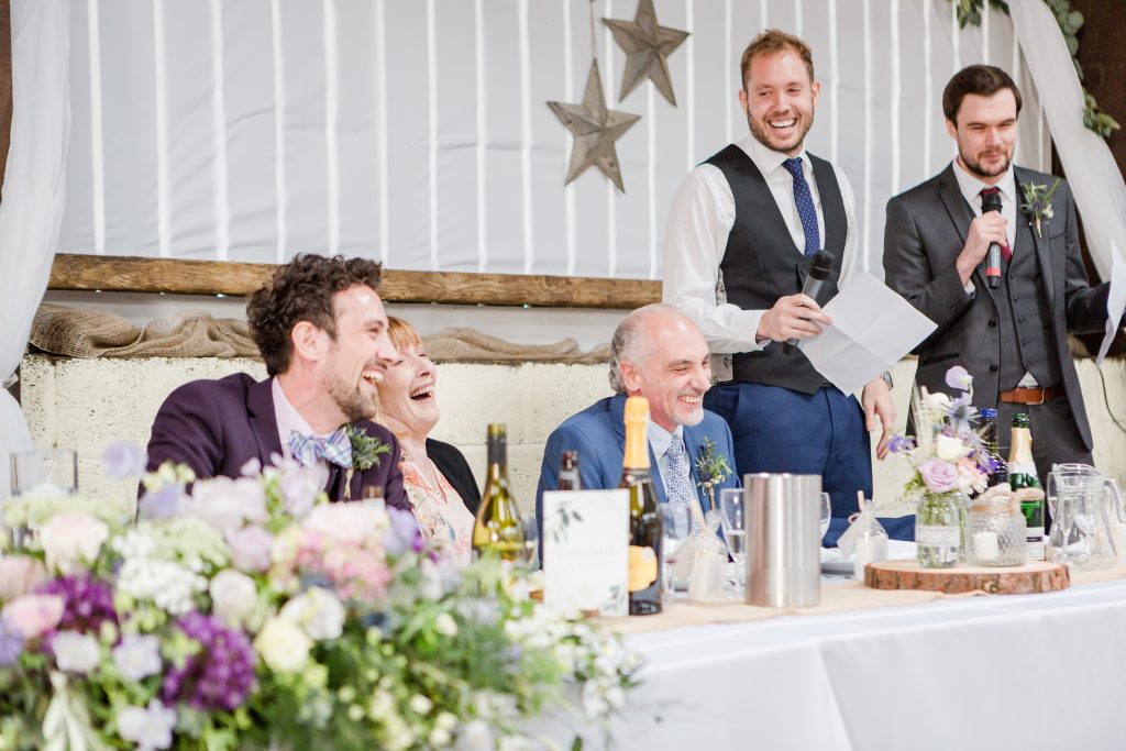 top table all laughing at two groomsmen giving speeches