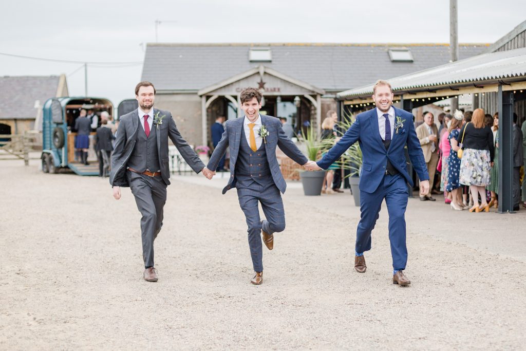 groom and his two bast-men skipping towards the camera with farm behind