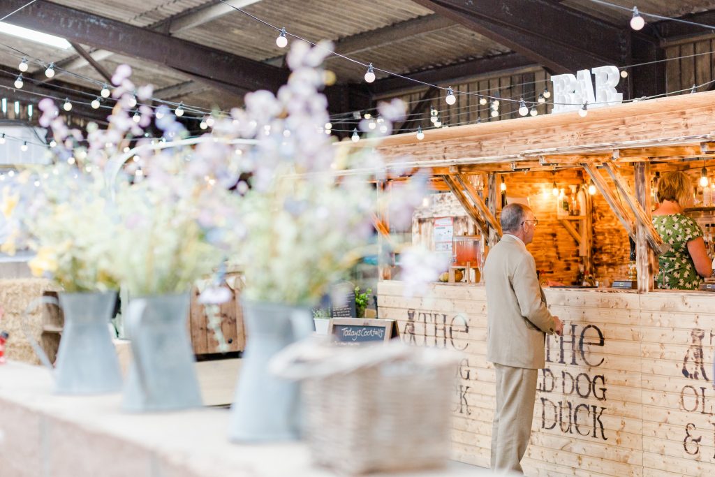 man ordering at wedding barn bar flowers in milk churn in foreground