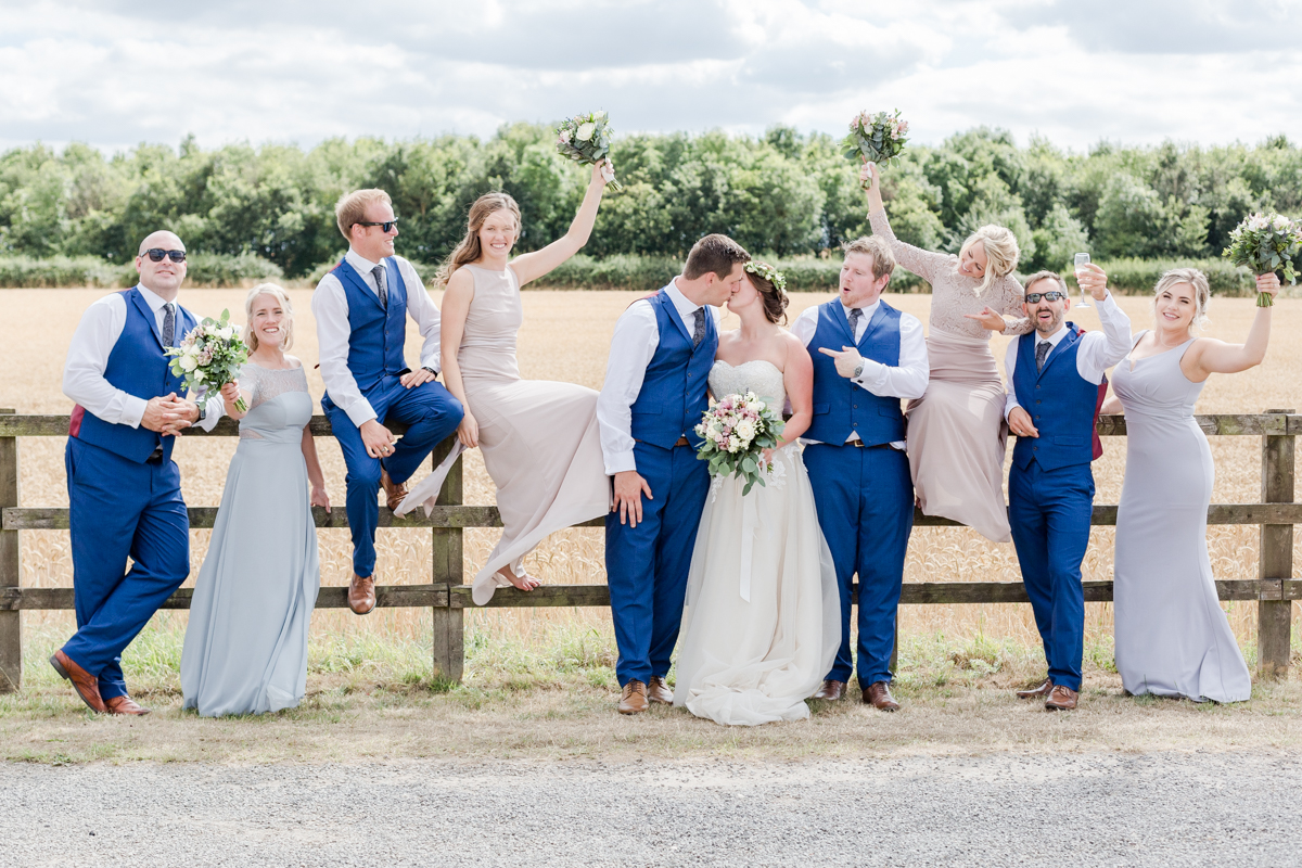 Bridal party sat on fence cheering the bride and groom kiss