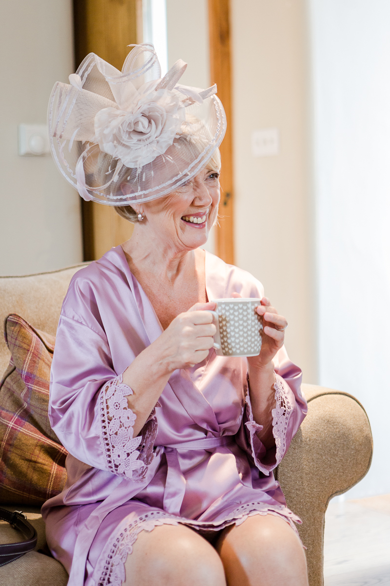 mother of bride wearing hat and purple satin dressing gown drinking tea