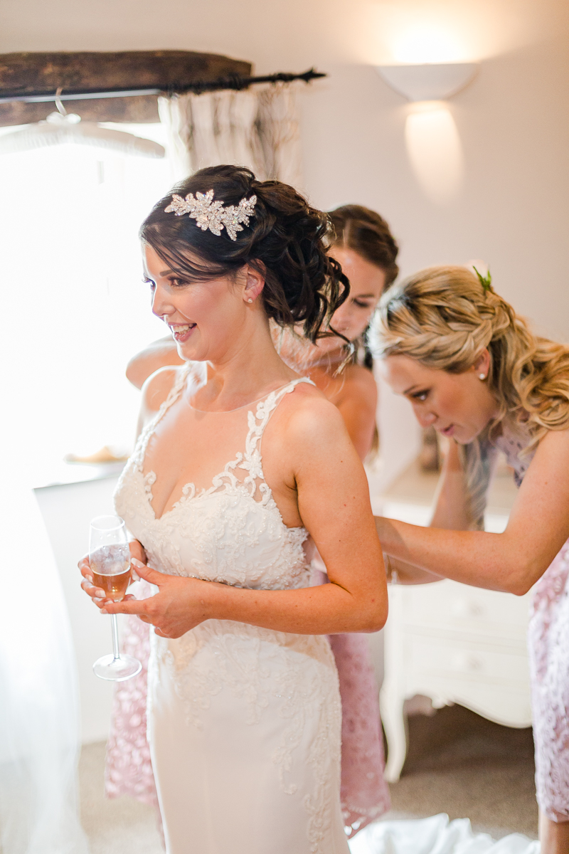 bridesmaids fastening back of brides dress