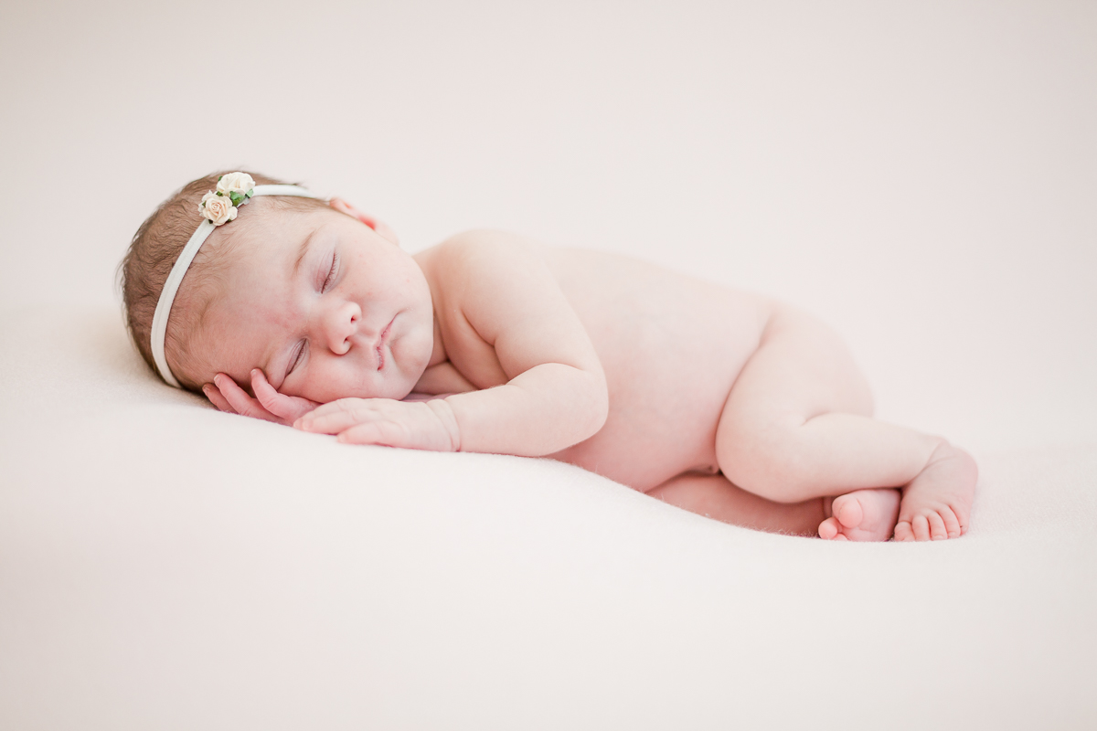 baby girl naked asleep on front with pink background