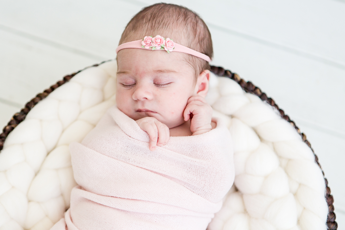 closeup of baby girl wrapped in pink asleep in round basket