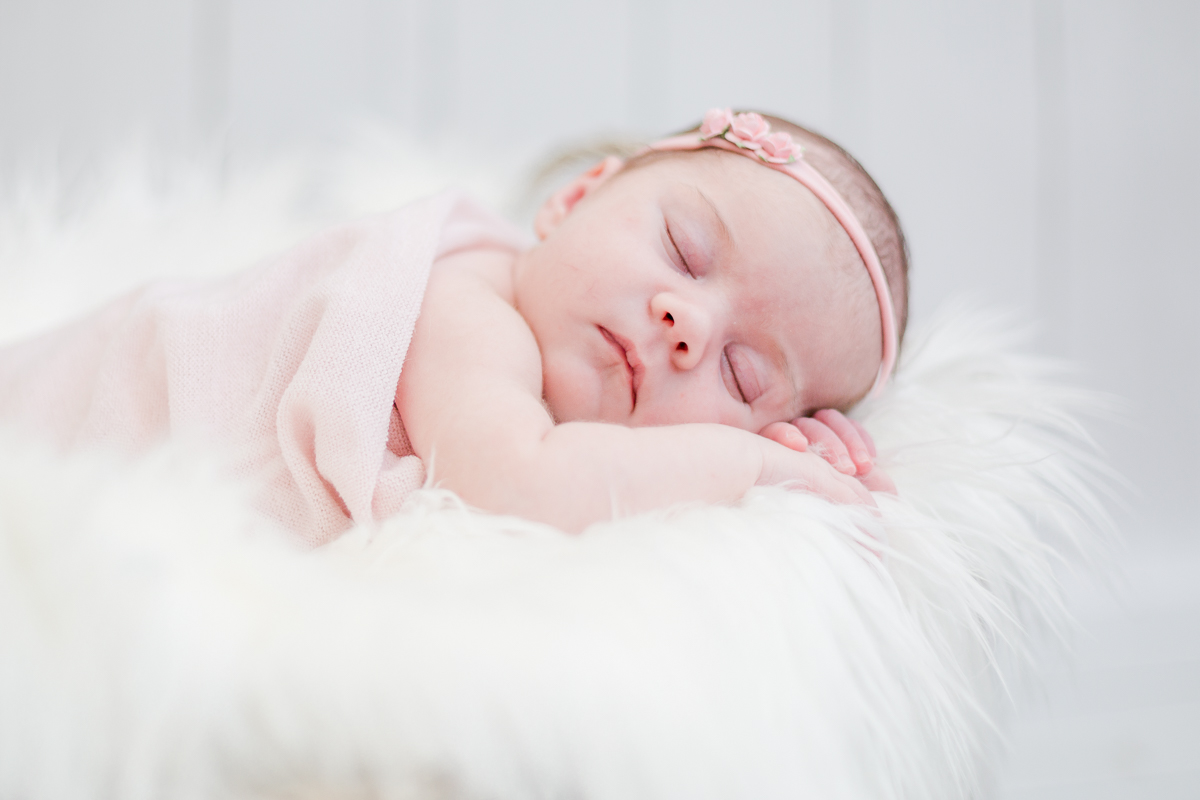 baby girl asleep on hands on white fur in basket