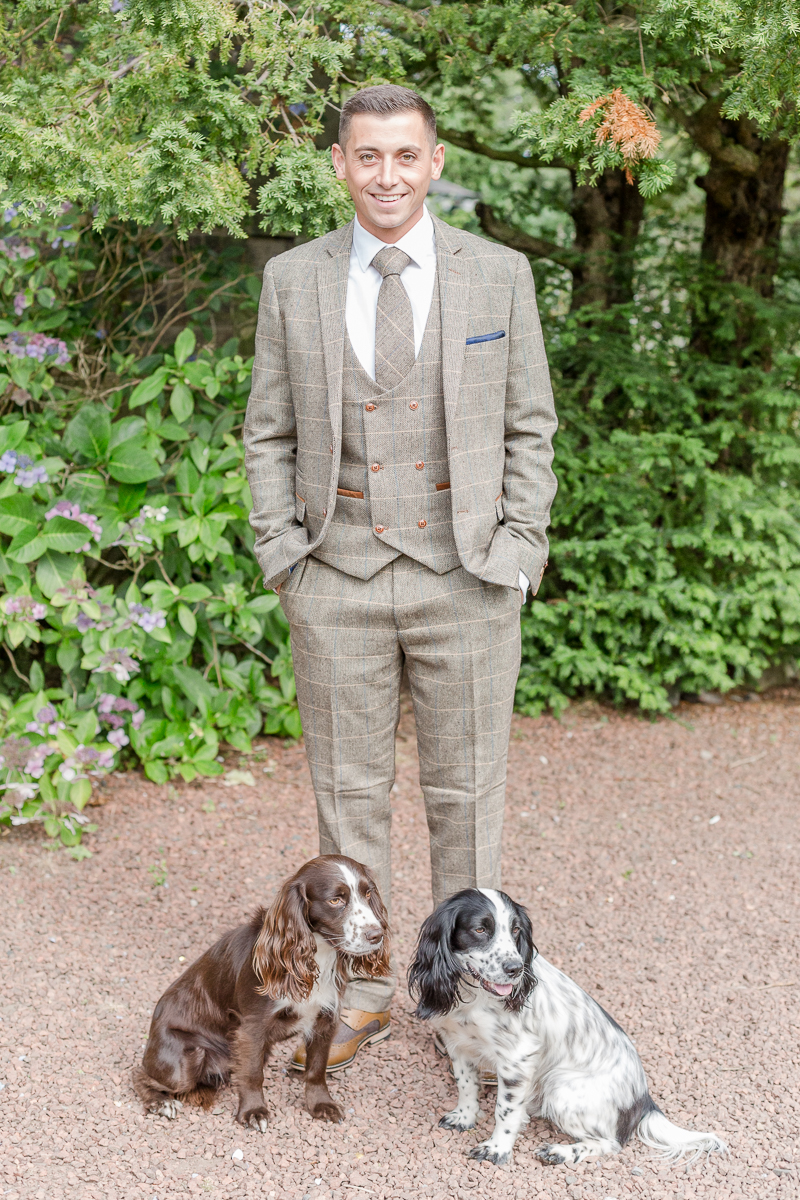 groom in tweed posing with two dogs