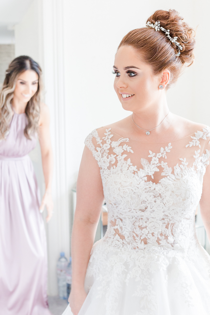 bride in lace wedding dress smiling to the side with bridesmaid in background