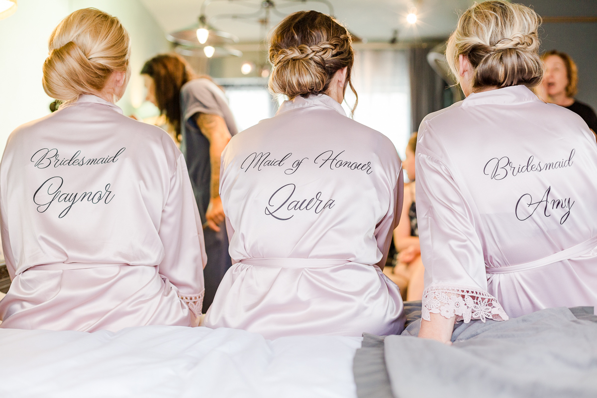 three bridesmaids sat on edge of bed wearing silk dressing gowns