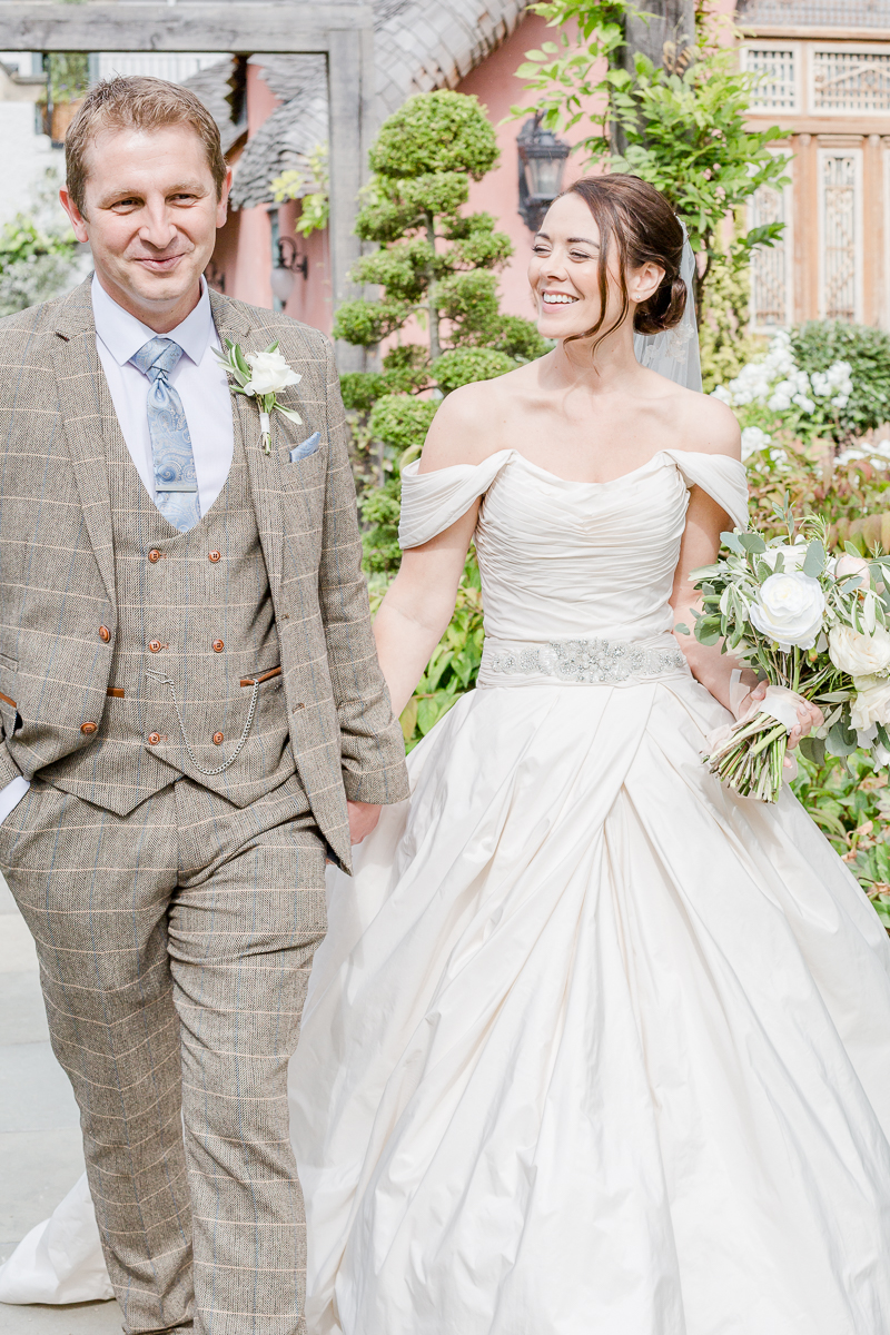 bride smiling at groom walking hand in hand through flowers