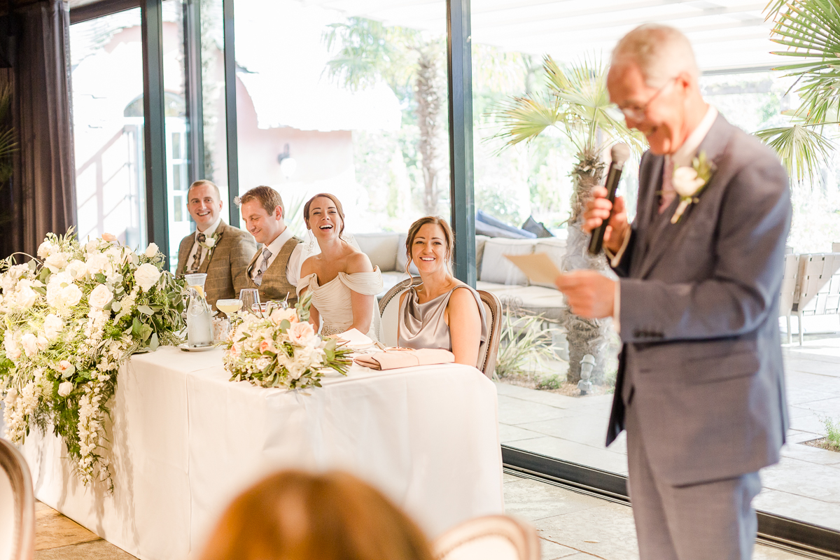 father of bride gives speech while bride and groom look on