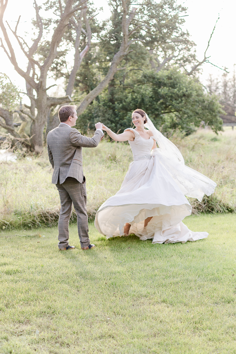 groom swirls bride in green field at sunset