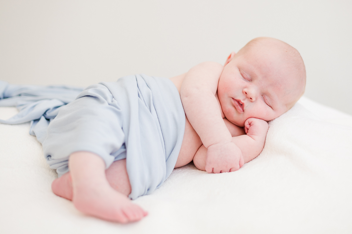 baby boy wrapped in blue asleep on side with head resting on hand