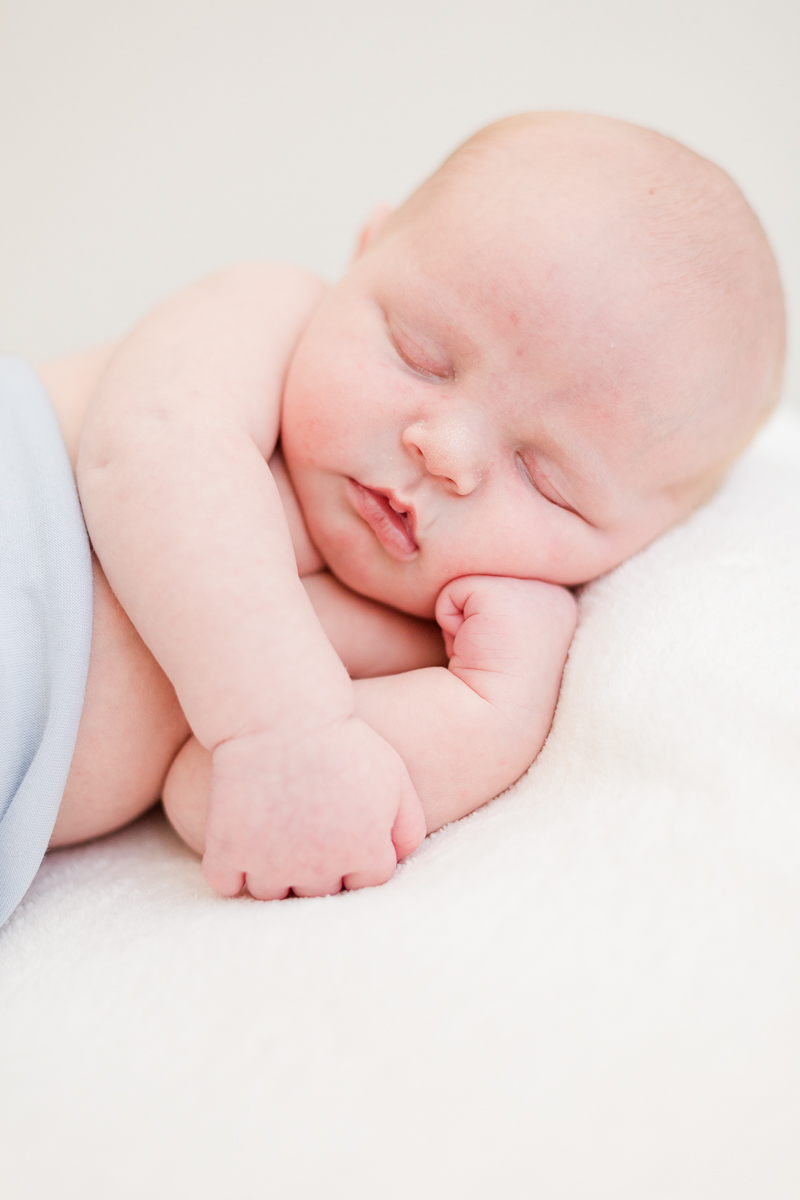 baby boy wrapped in blue asleep on side with head resting on hand close up