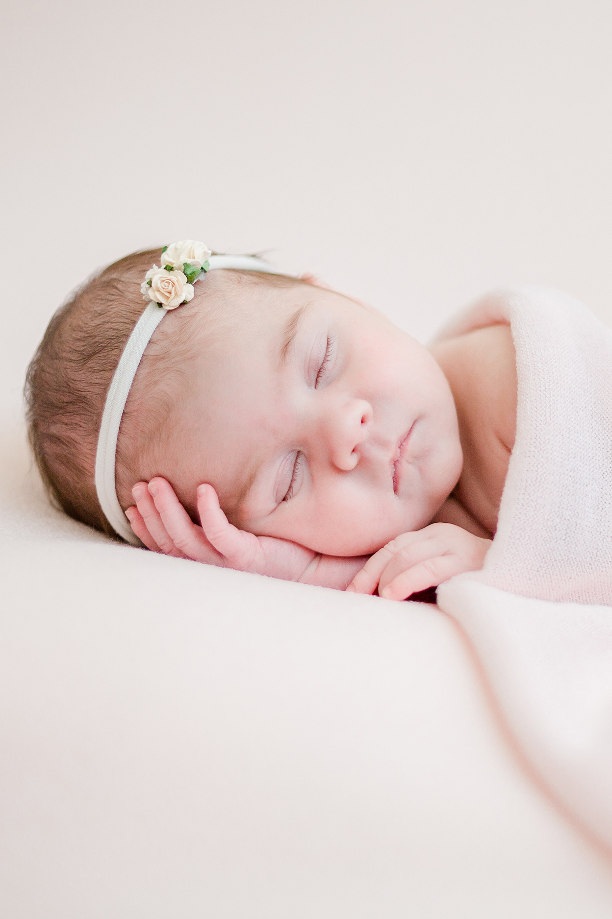 newborn baby girl asleep on her side head on hand under pink blanket