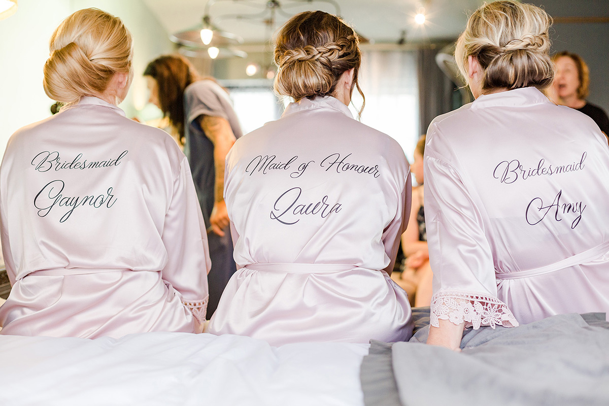 three bridesmaids sitting on bed with silk dressing gowns