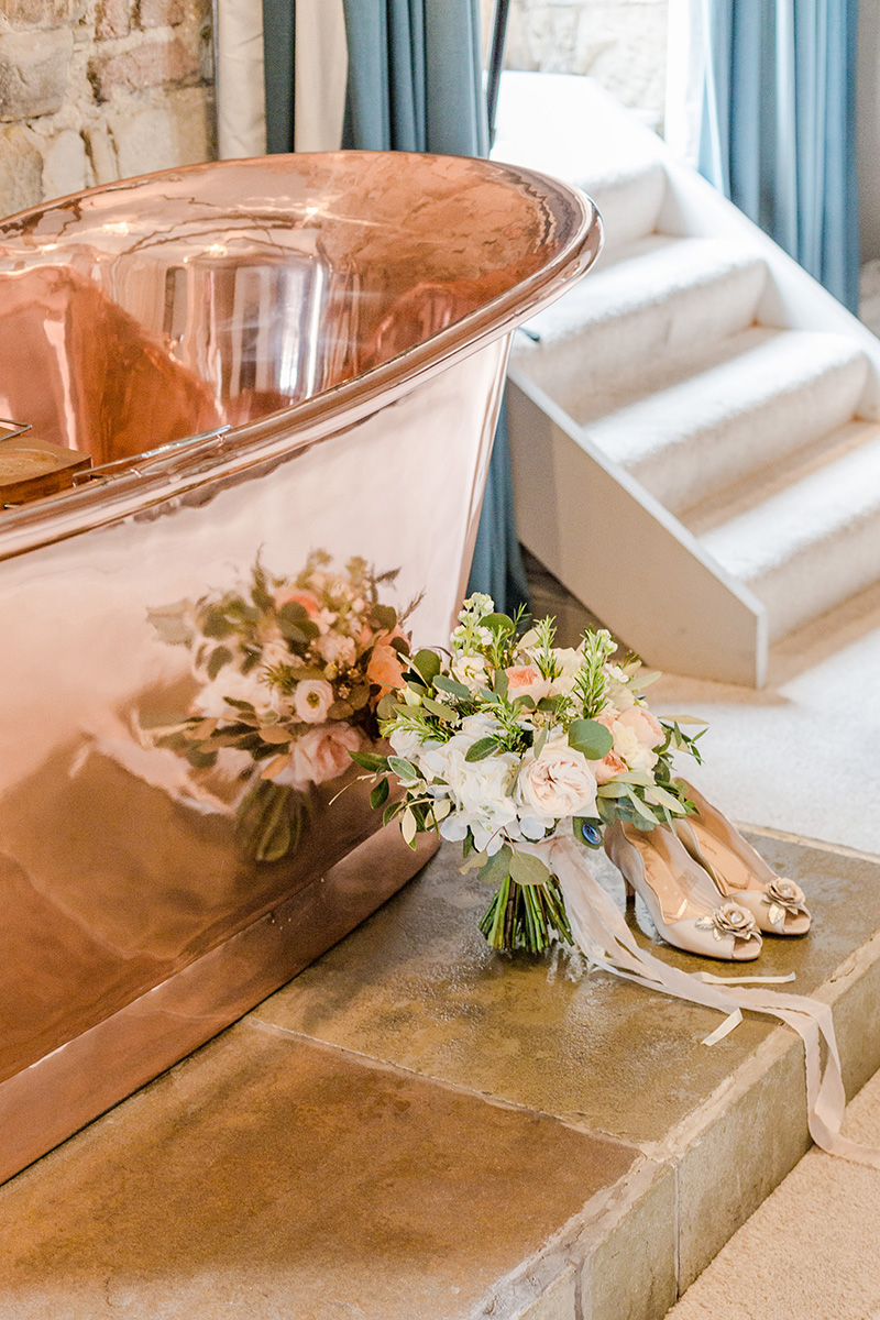 bouquet and wedding shoes next to shiny copper bath