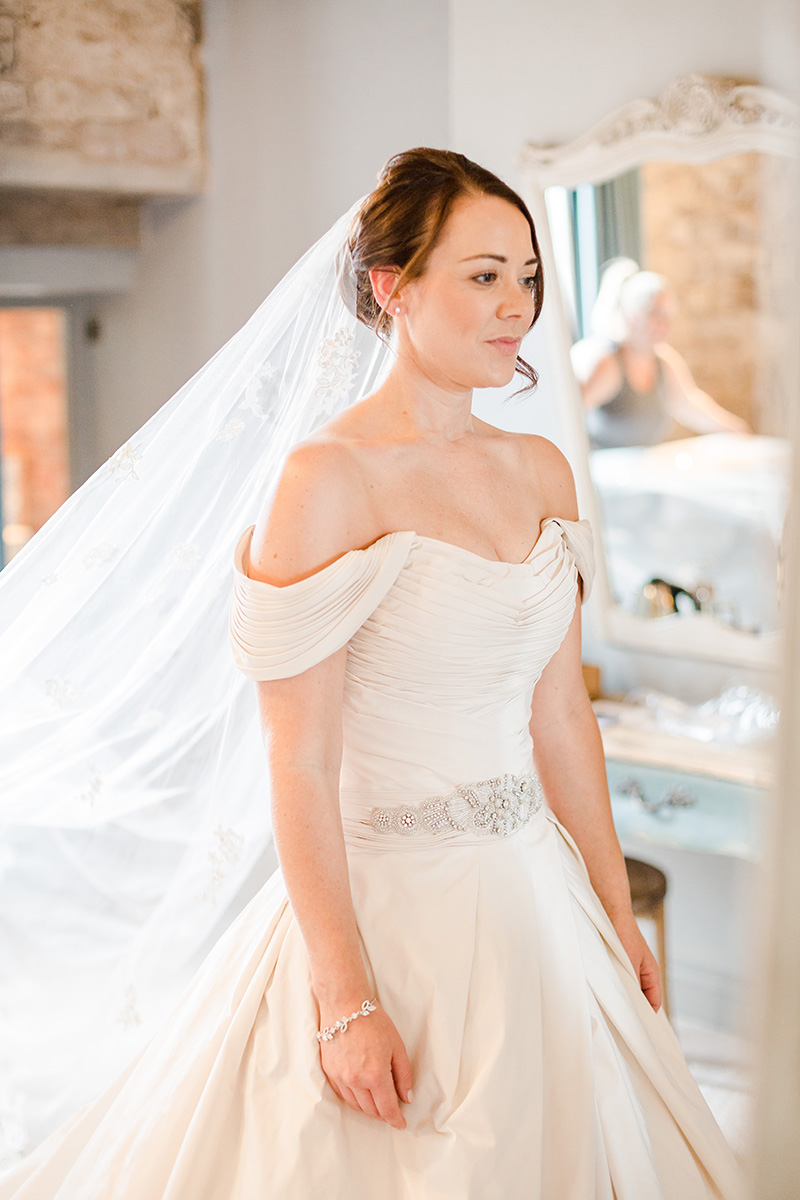 bride in gown and veil looking emotional in mirror