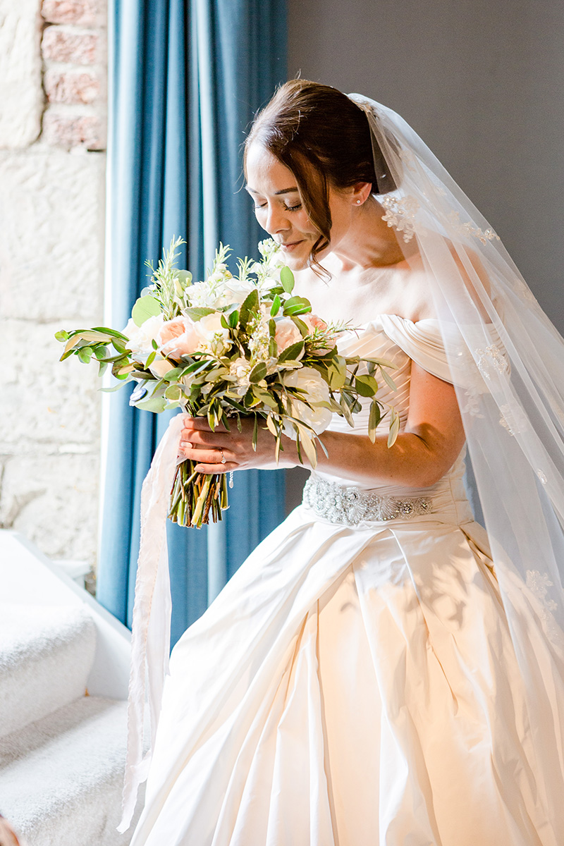 bride stood in balcony window smelling bouquet