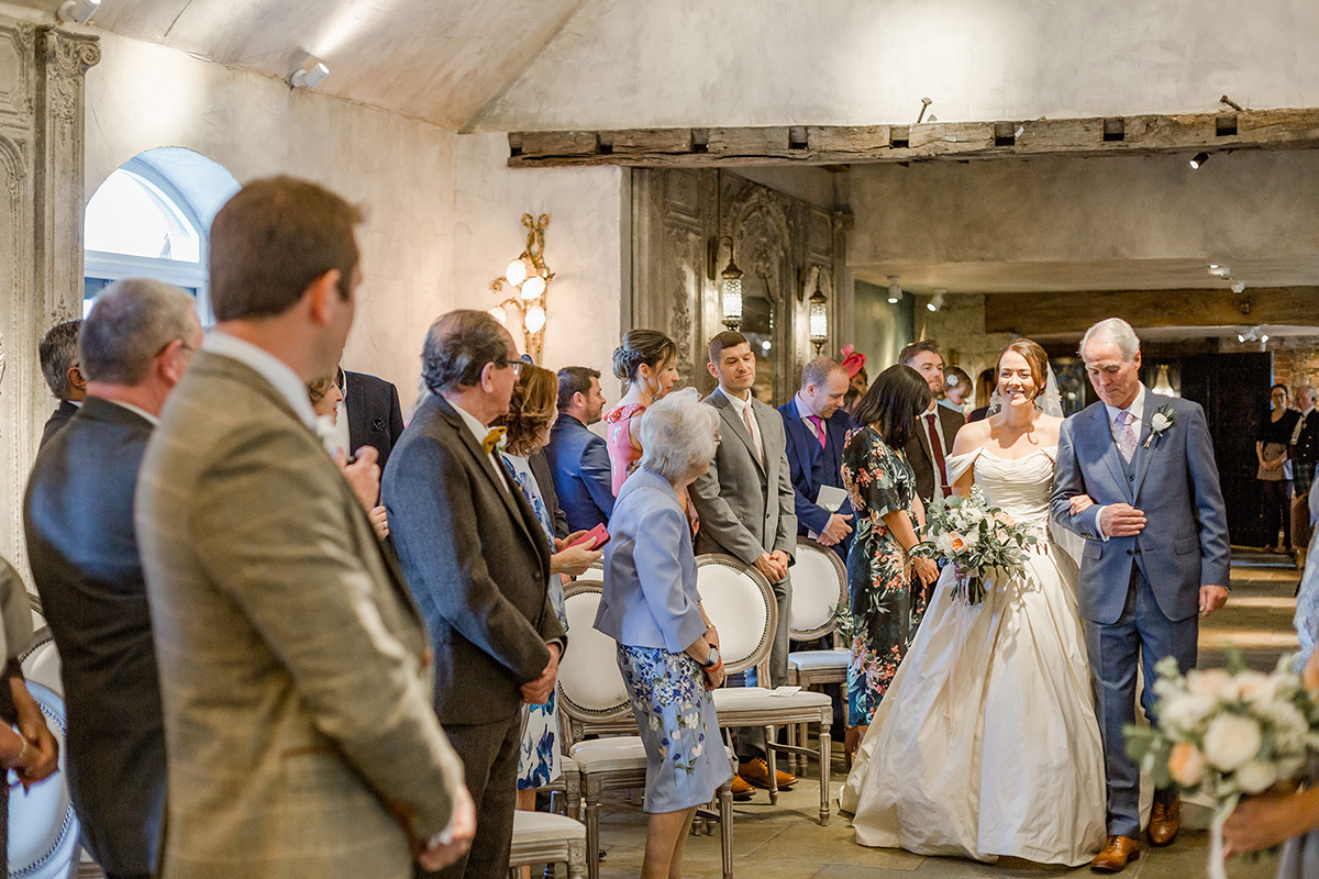 groom watches bride and father of bride walk towards him