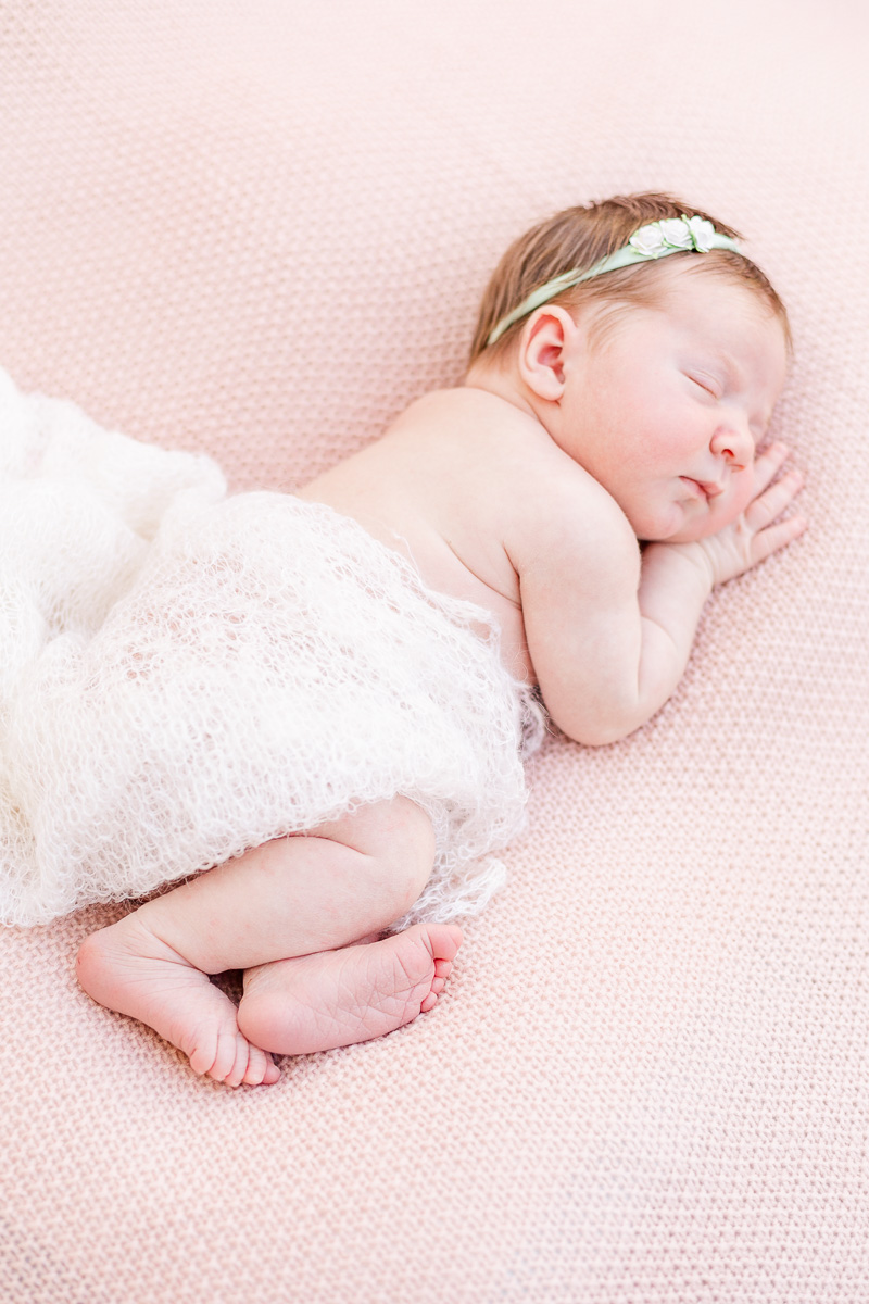 newborn baby asleep on her side on pink blanket wrapped in white lace