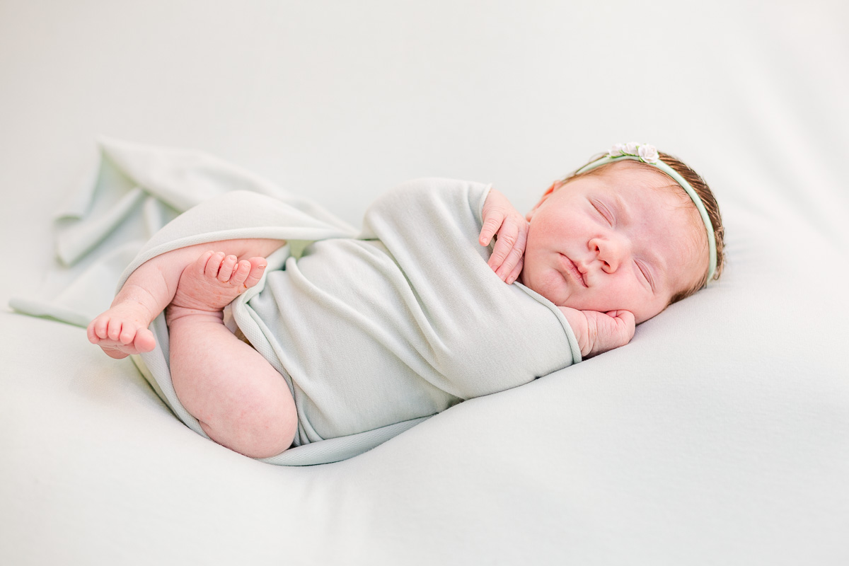 newborn baby girl asleep on back wrapped in mint green blanket