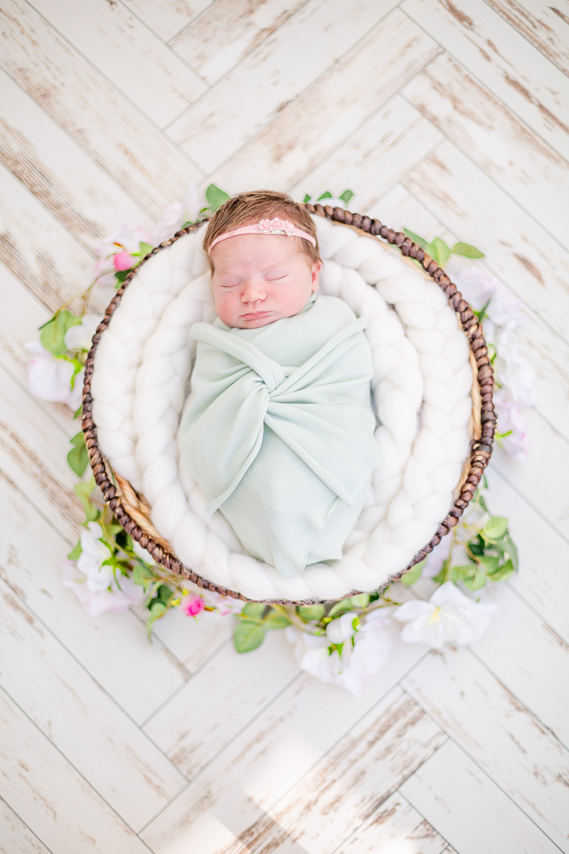 newborn baby girl asleep in round basket with mint green wrap