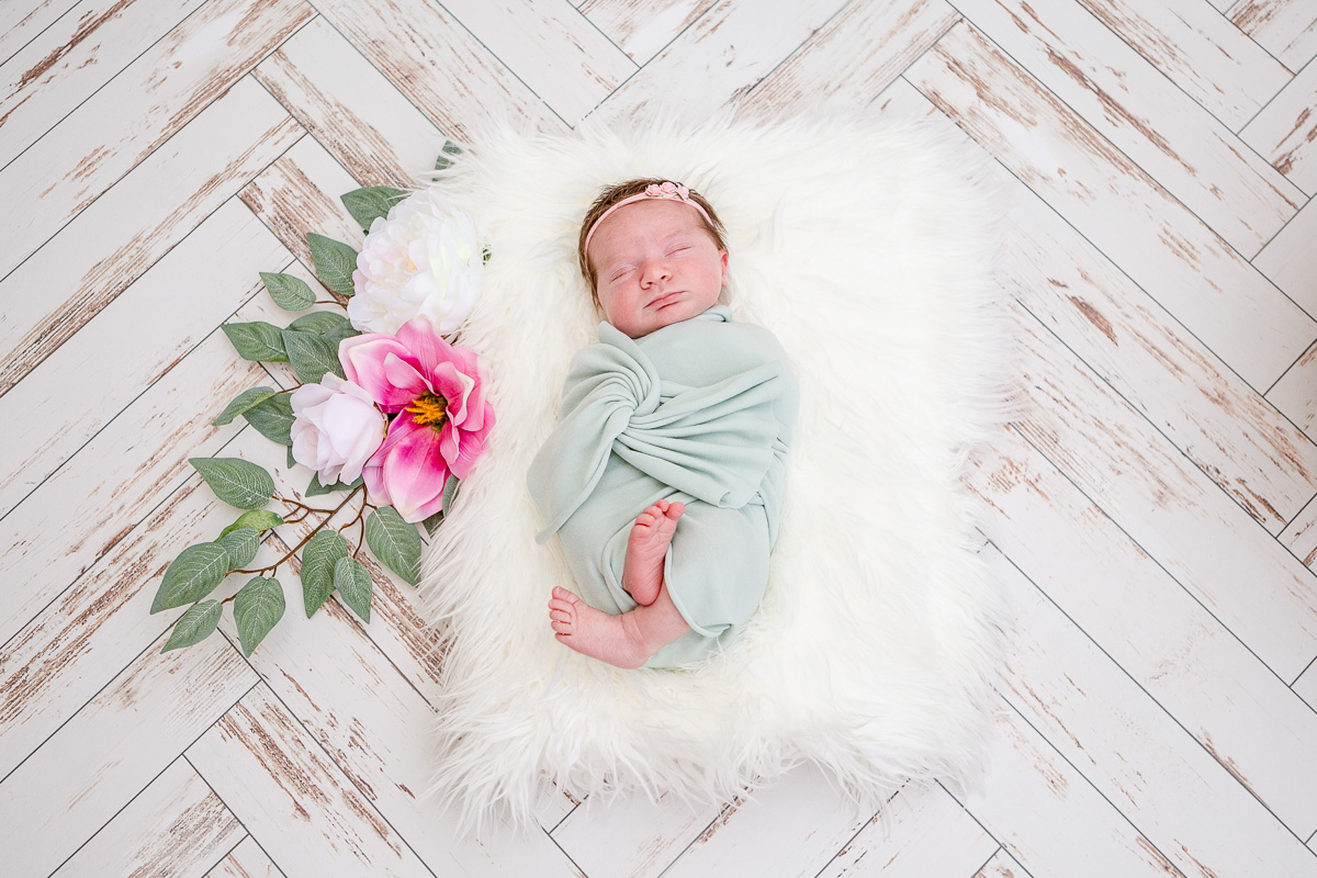 newborn baby girl asleep on white fur with flower garland