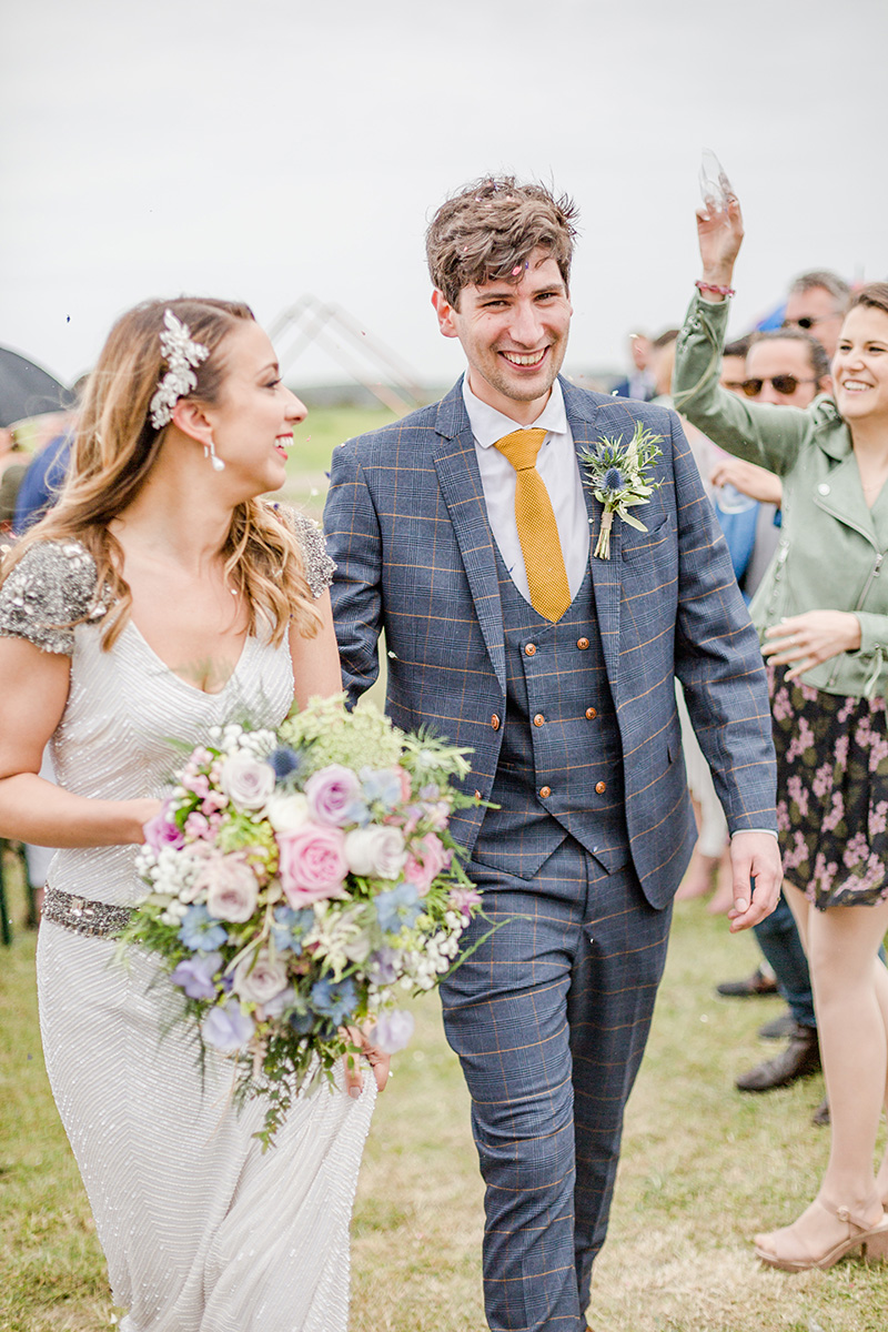 bride and groom walking through field smiling