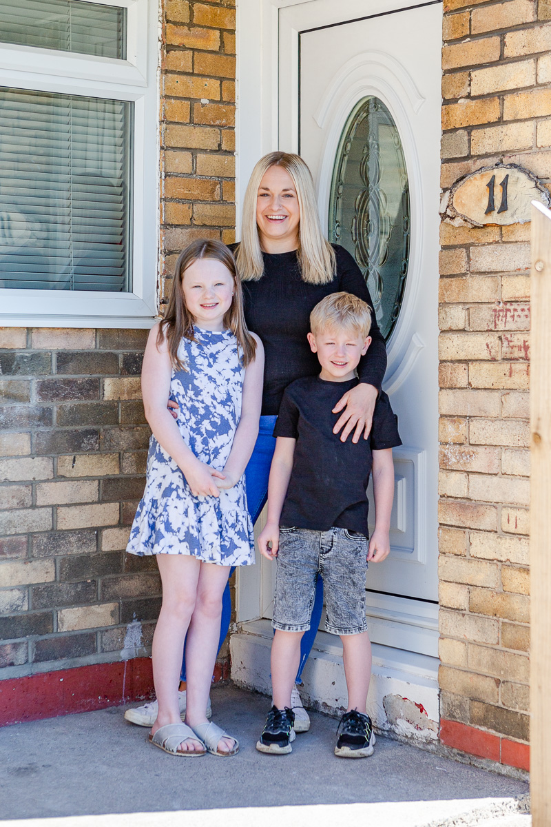 a mummy stood on doorstep with arms around daughter and son