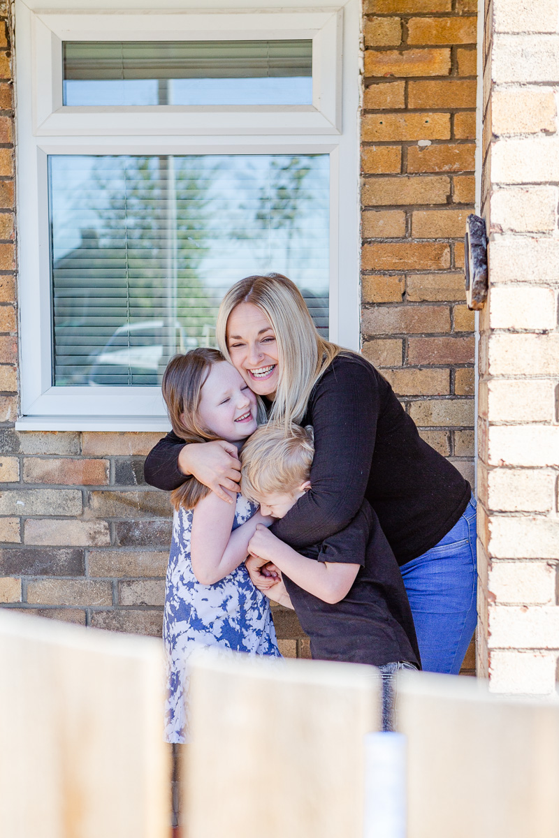 a mummy cuddling daughter and son on doorstep