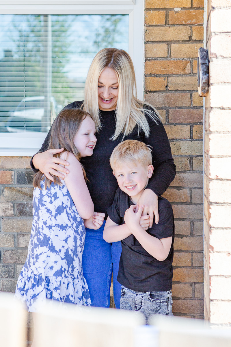 a mummy with arms around daughter and son on doorstep