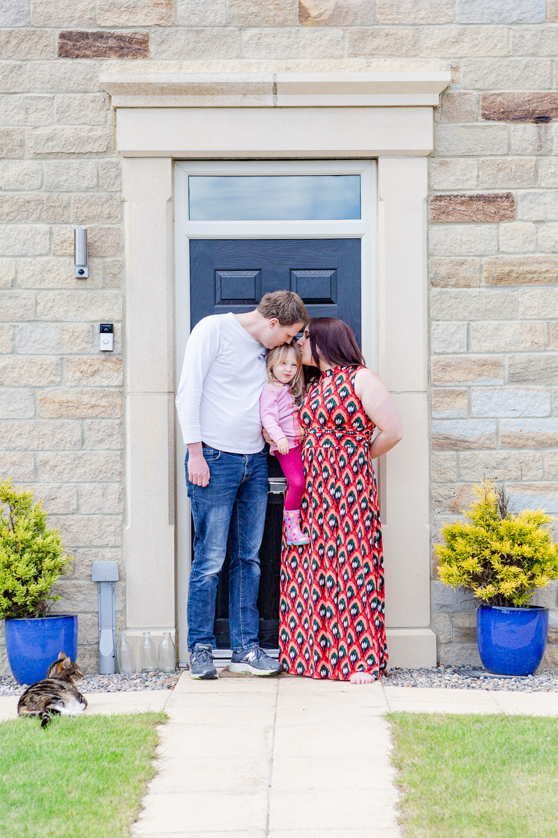 a mummy and daddy kissing daughter on doorstep