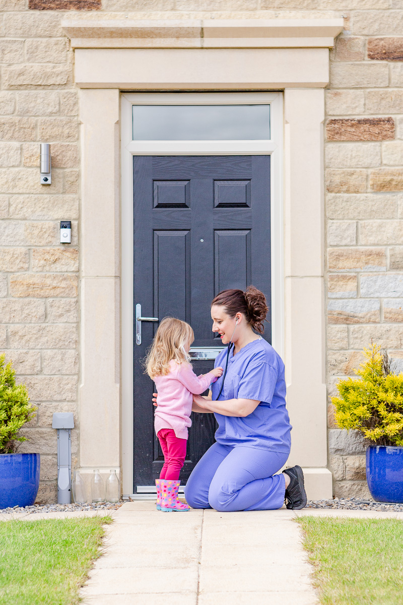 a mummy in NHS scrubs bending down listening to daughters heart on doorstep