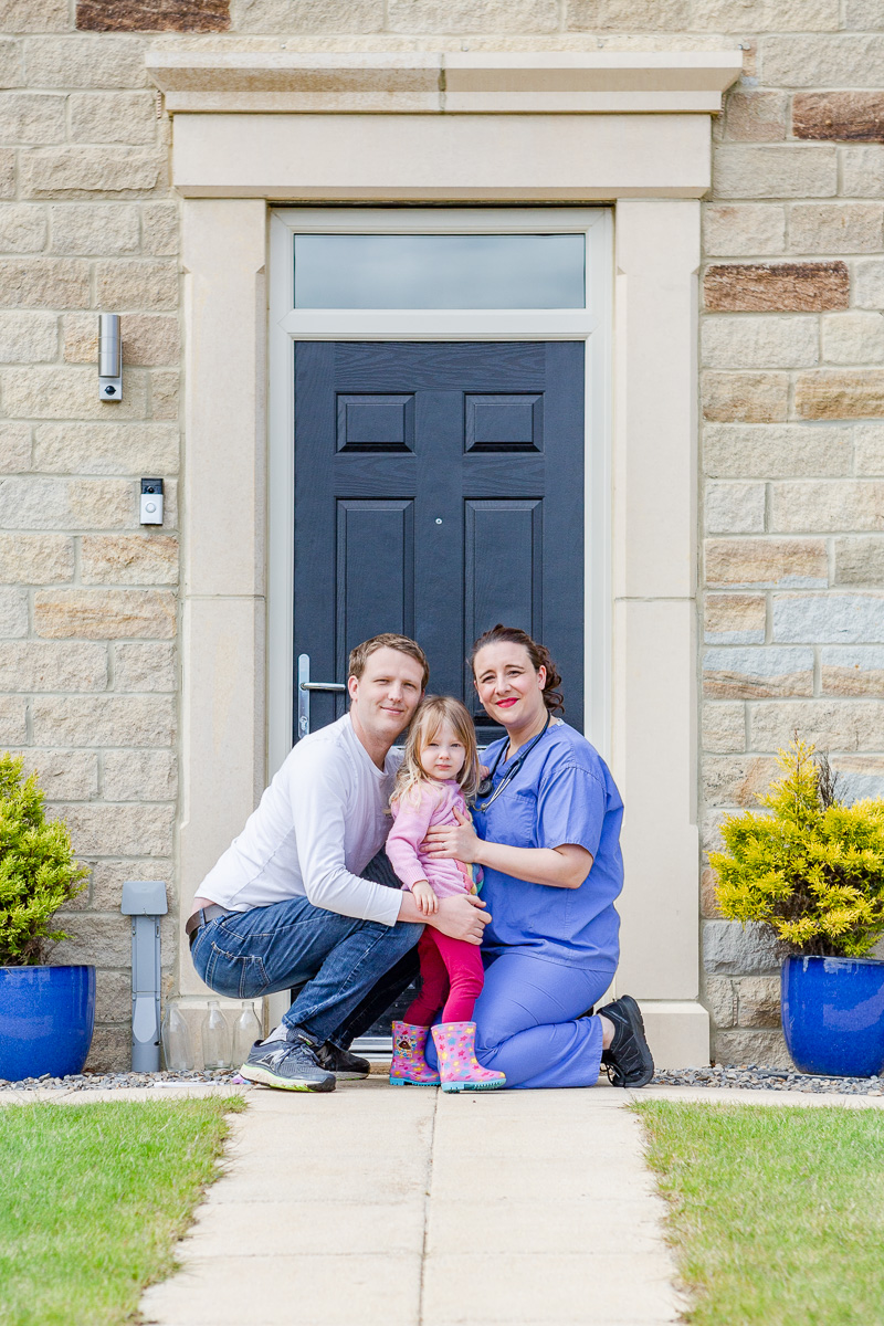 a mummy in scrubs with husband and daughter on doorstep