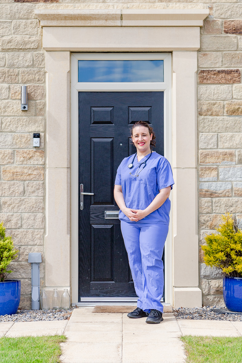 a lady doctor stood on doorstep in scrubs