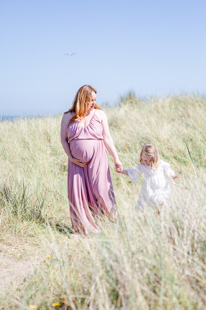 mummy holding hands with daughter walking through dunes