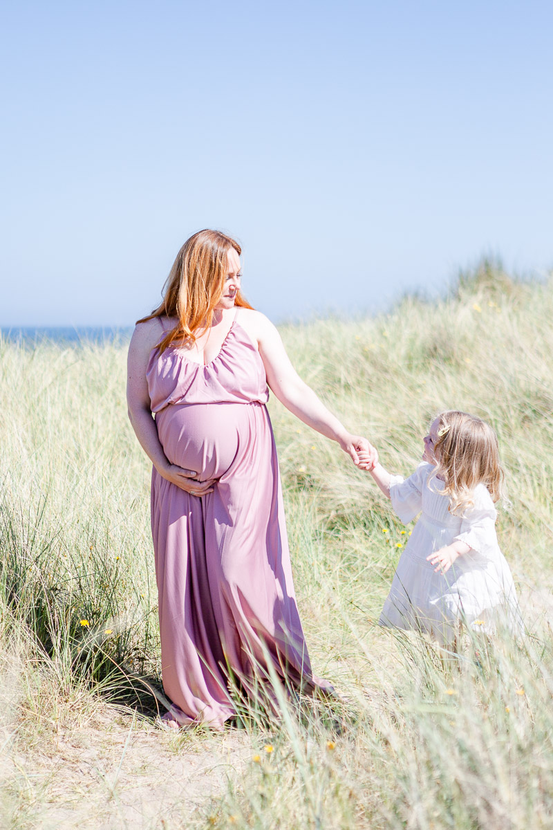 pregnant mummy walking through dunes holding daughters hand