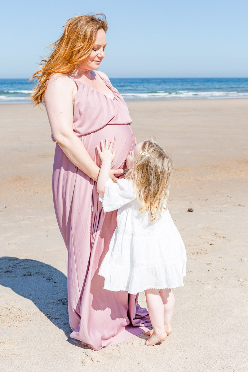 toddler kissing mummy's pregnancy tummy on beach