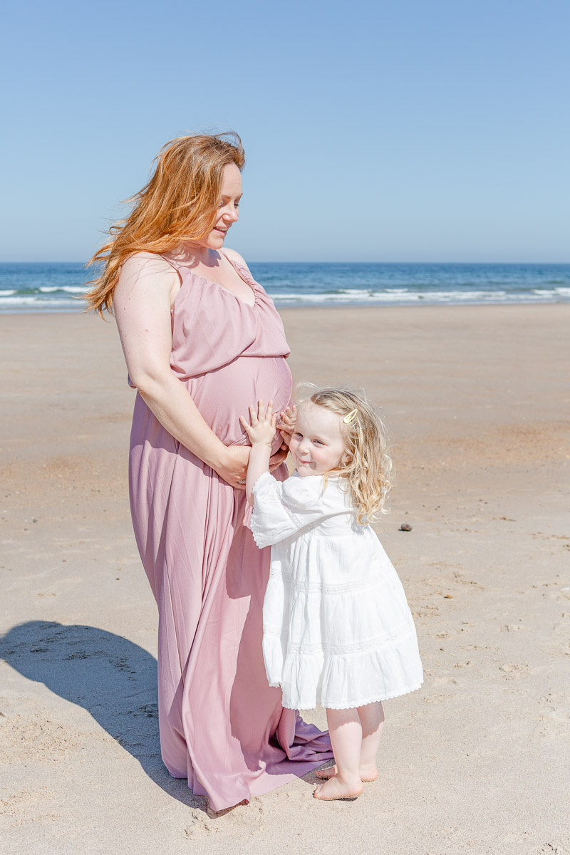 toddler holding mummy's pregnancy tummy on beach