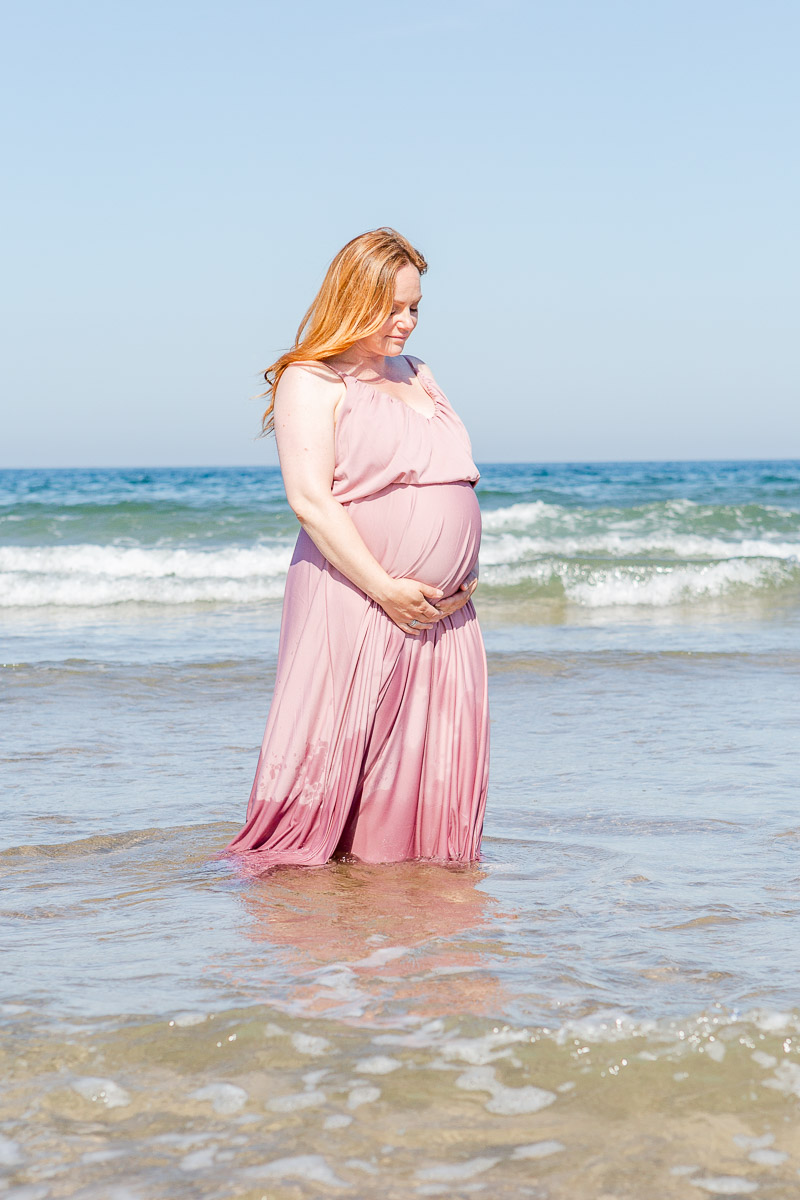 pregnant mummy in pink maxi dress paddling in sea holding bump